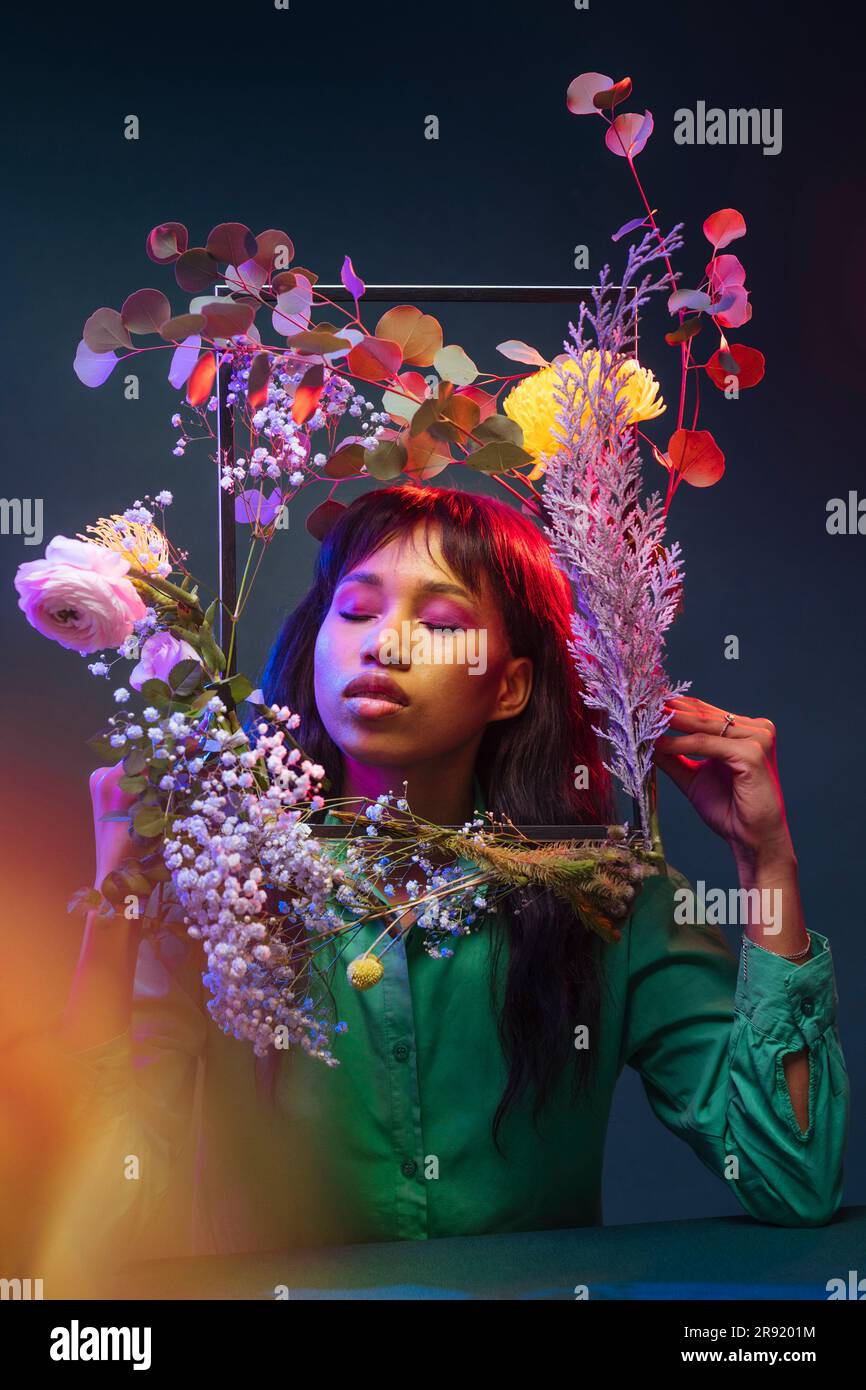 Donna con gli occhi chiusi che regge una cornice di fiori colorati Foto Stock