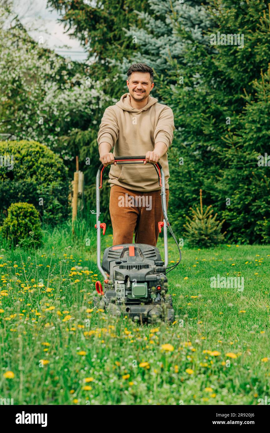 Uomo sorridente in piedi con il rasaerba in giardino Foto Stock