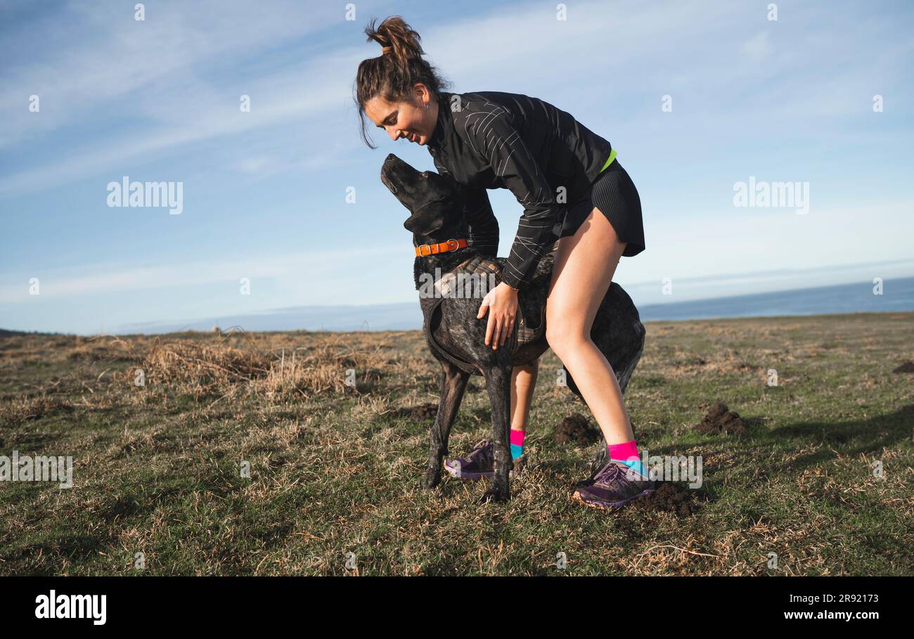 Donna sorridente che accarezza il cane sull'erba Foto Stock