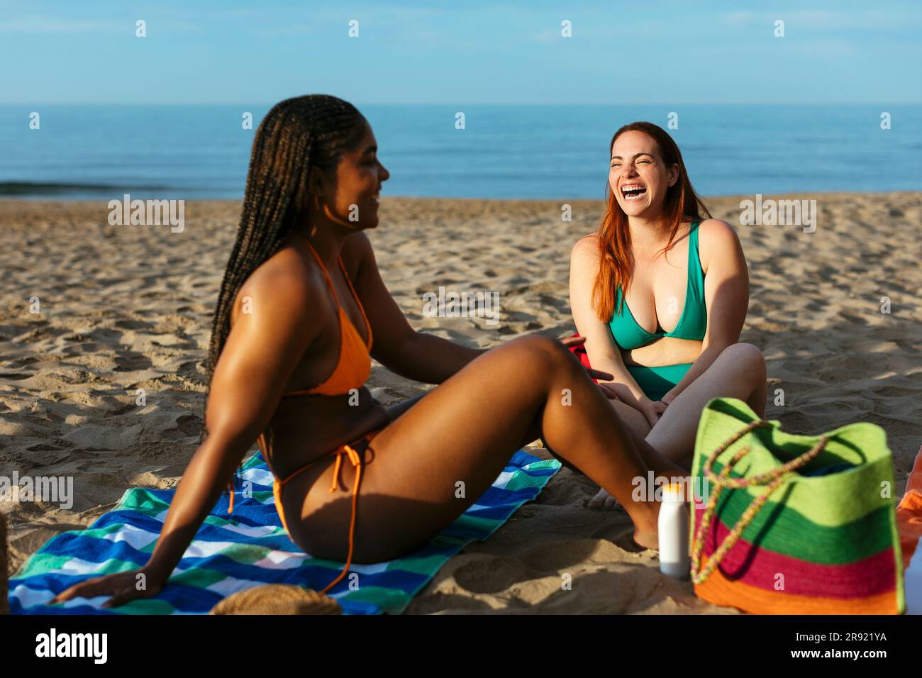 Una donna felice che ride con un amico seduto in spiaggia Foto Stock