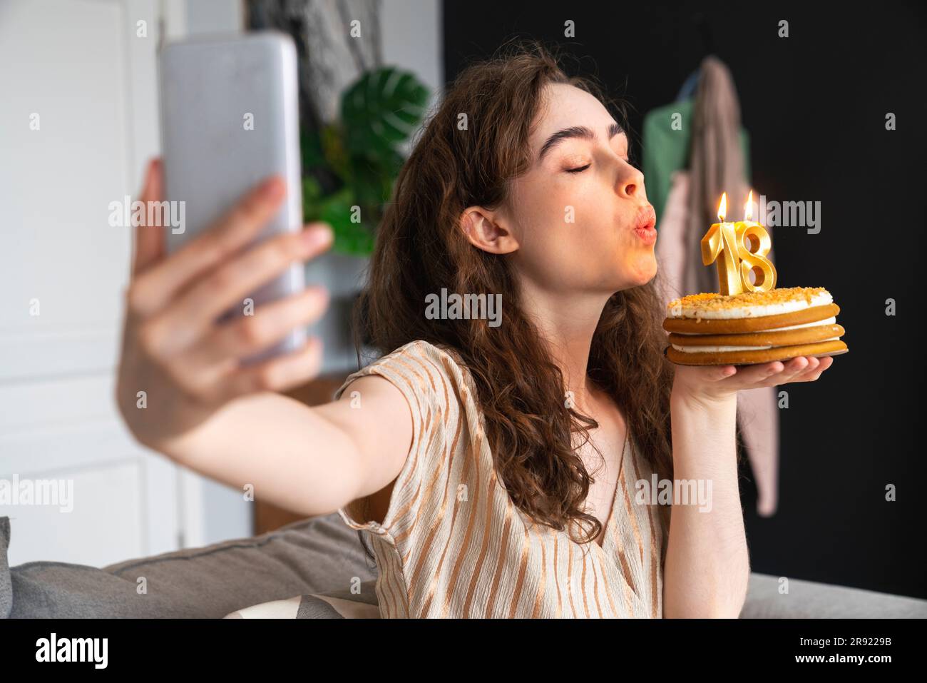 Giovane donna che soffia la candela sulla torta di compleanno e si fa selfie a casa Foto Stock
