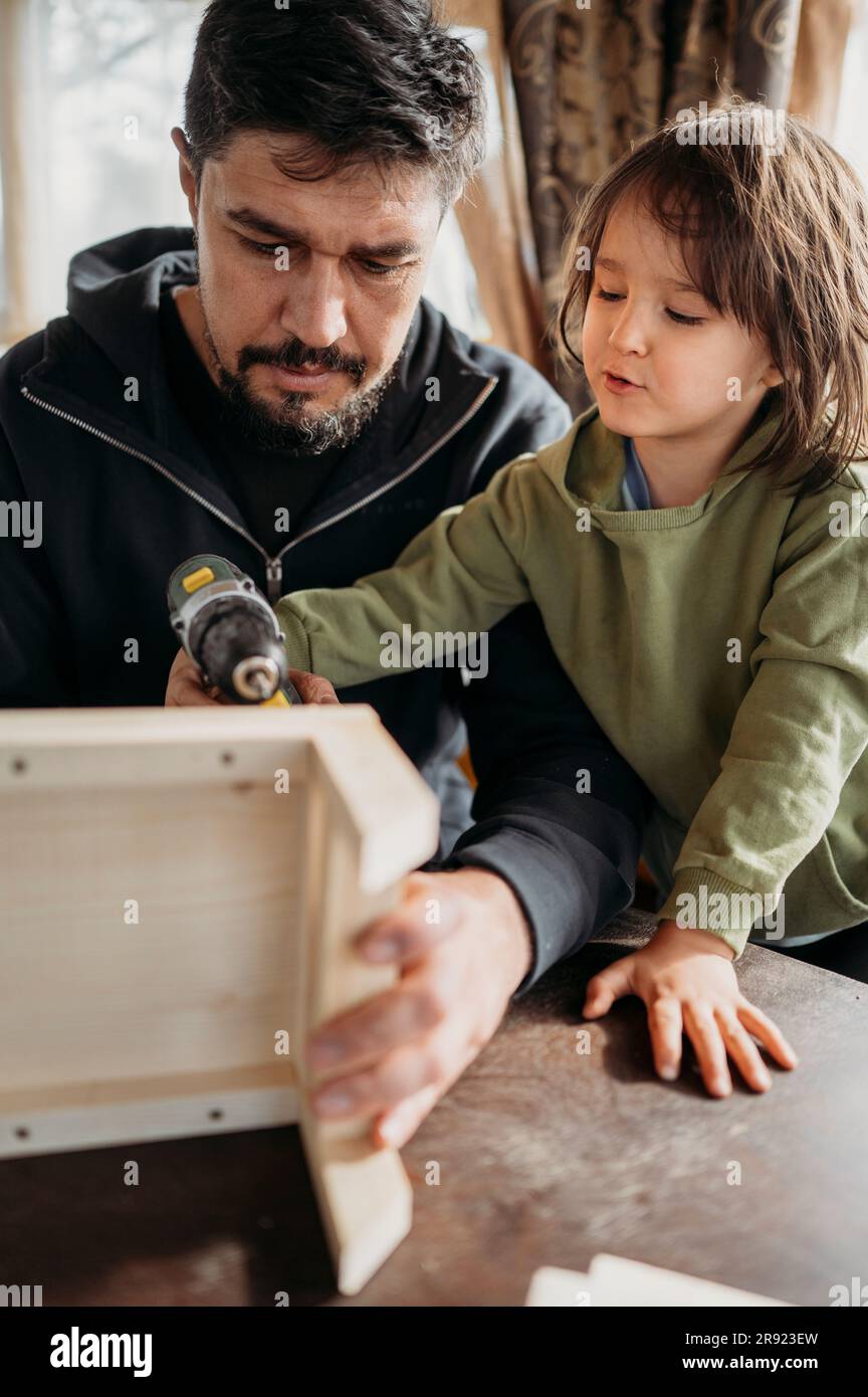 Figlio che sta imparando a costruire una casa per gli uccelli con il padre a casa Foto Stock