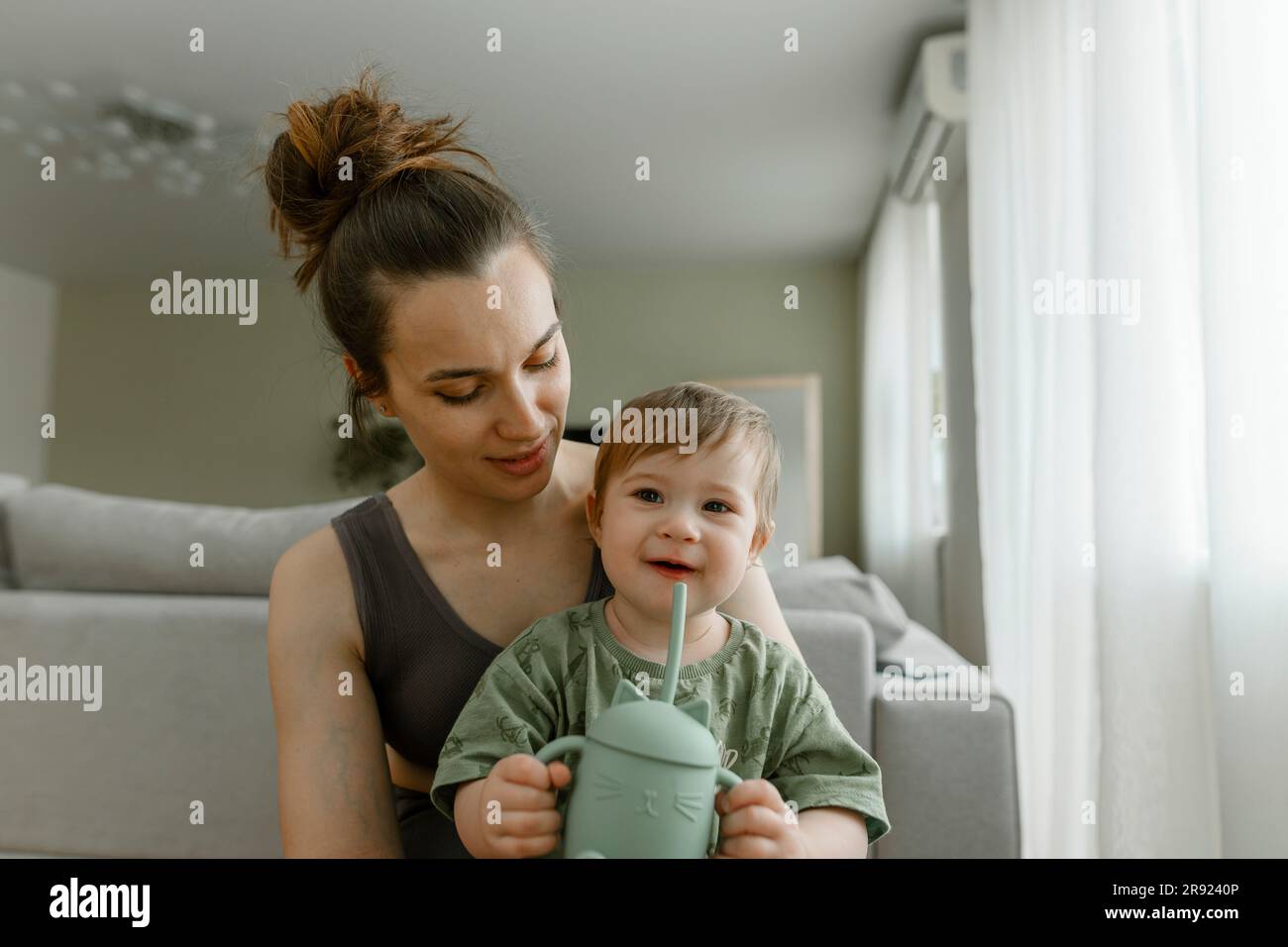 Madre seduta con una figlia che tiene a casa il biberon Foto Stock