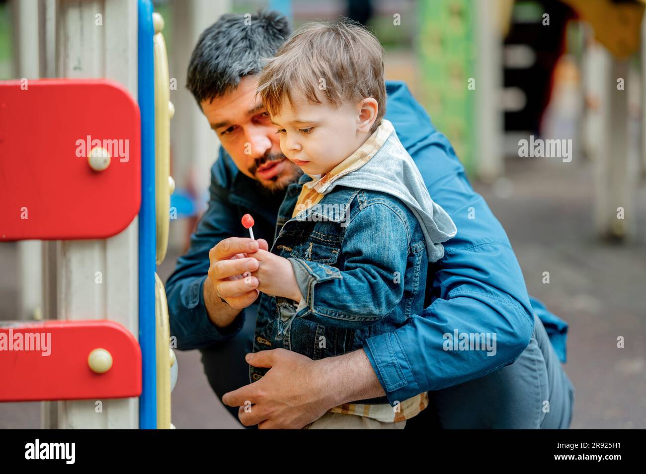 Padre che dà lecca lecca al figlio al parco giochi Foto Stock