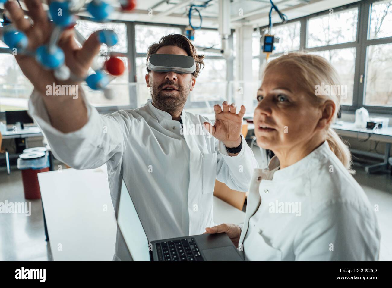 Scienziato che indossa un simulatore di realtà virtuale che esamina la struttura molecolare con un collega Foto Stock