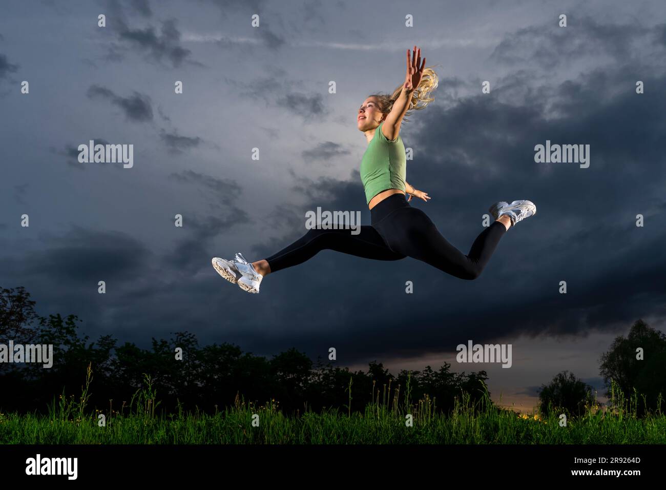 Atleta con le braccia allungate saltando al crepuscolo Foto Stock