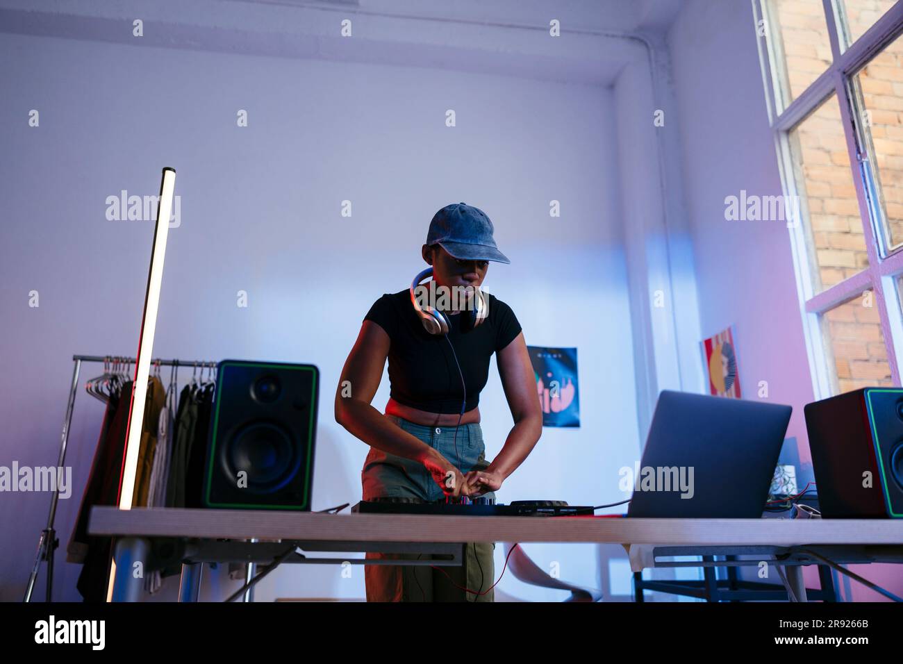 Giovane DJ che utilizza un computer portatile e un mixer audio funzionante a casa Foto Stock