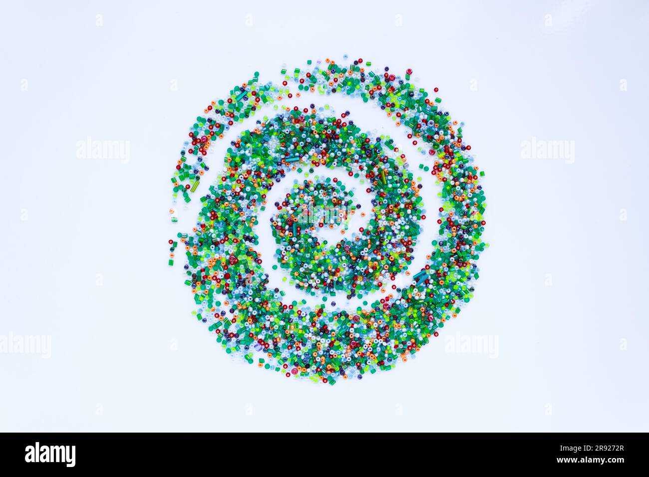 Su uno sfondo bianco, un motivo di piccole perle colorate a forma di spirale. Foto Stock