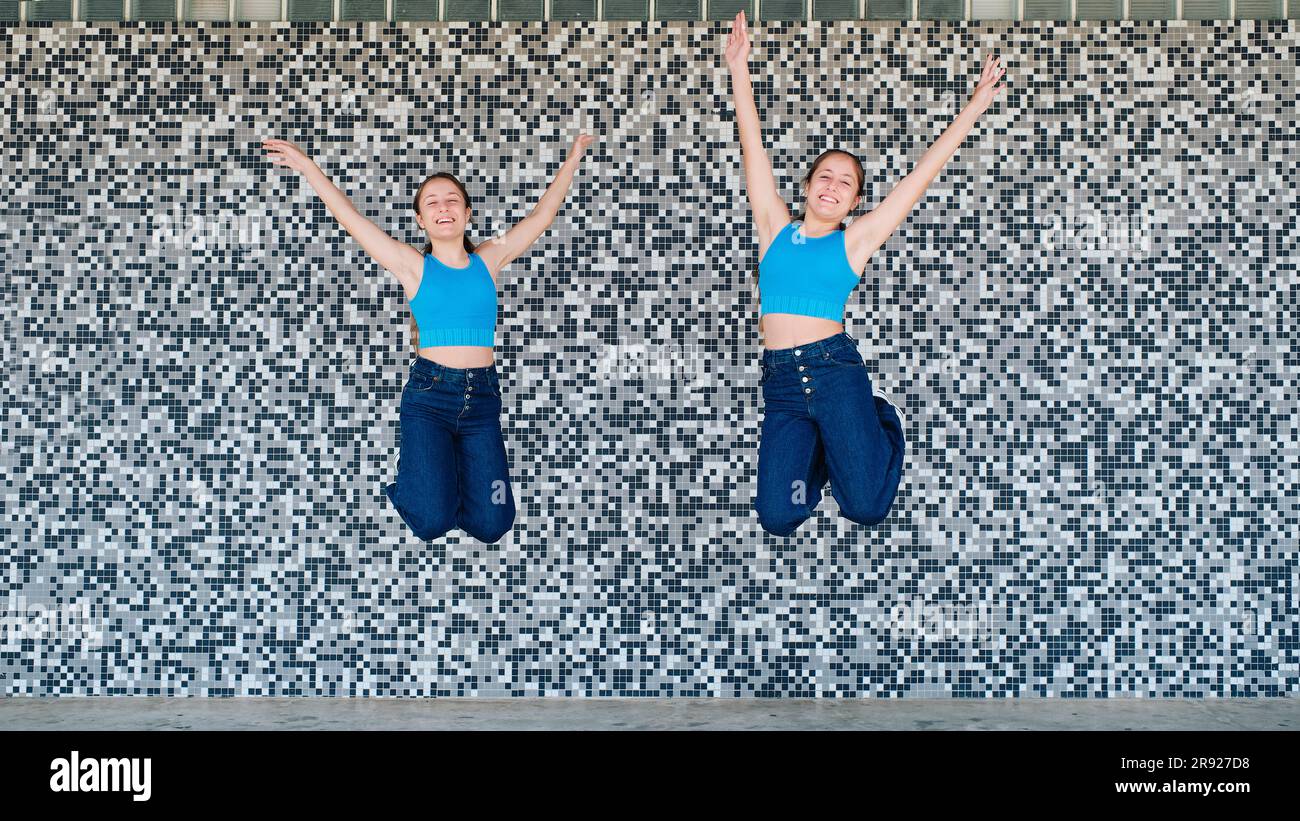 Sorelle felici che saltano davanti a un muro con texture Foto Stock
