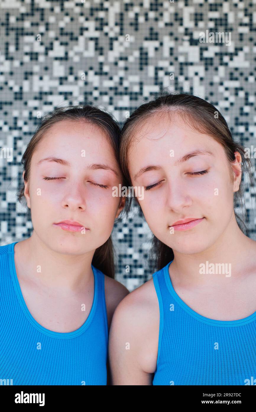 Sorelle gemelle con gli occhi chiusi davanti al muro testurizzato Foto Stock