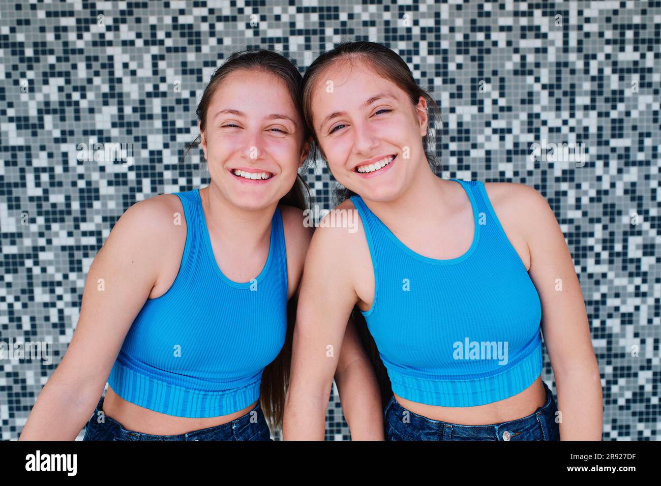 Sorelline gemelle felici di fronte a un muro con texture Foto Stock