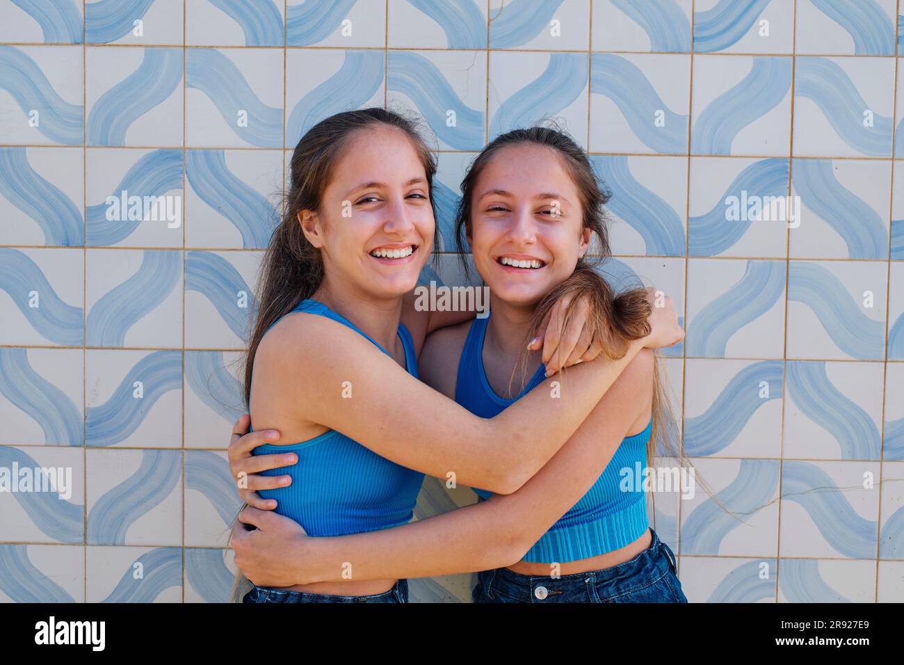 Sorelle gemelle che si abbracciano davanti al muro Foto Stock