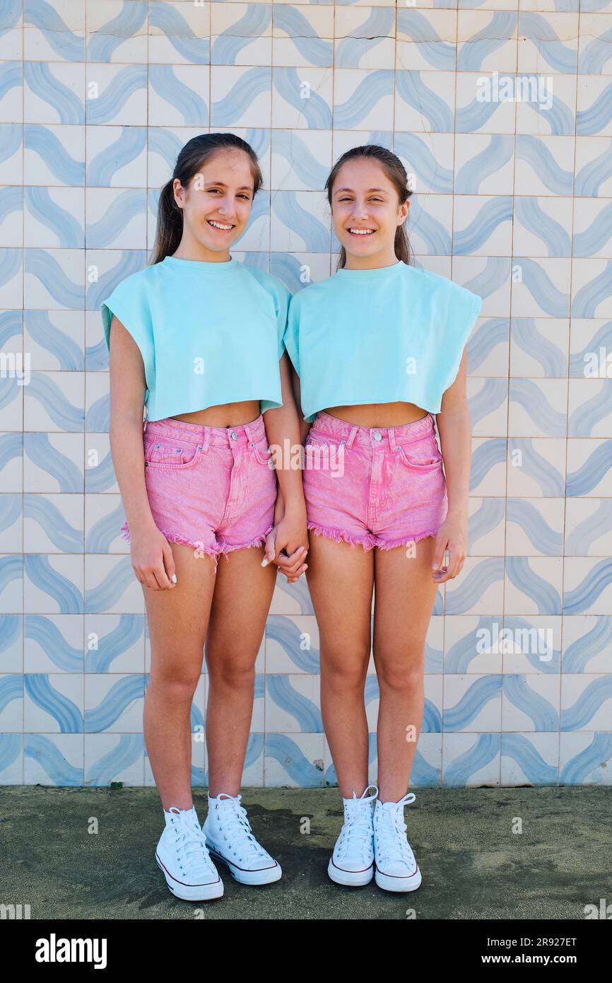 Sorelle gemelle felici in piedi insieme di fronte al muro modellato Foto Stock