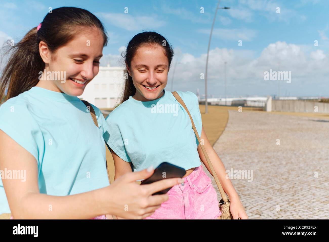 Sorelle gemelle felici che usano lo smartphone nelle giornate di sole Foto Stock