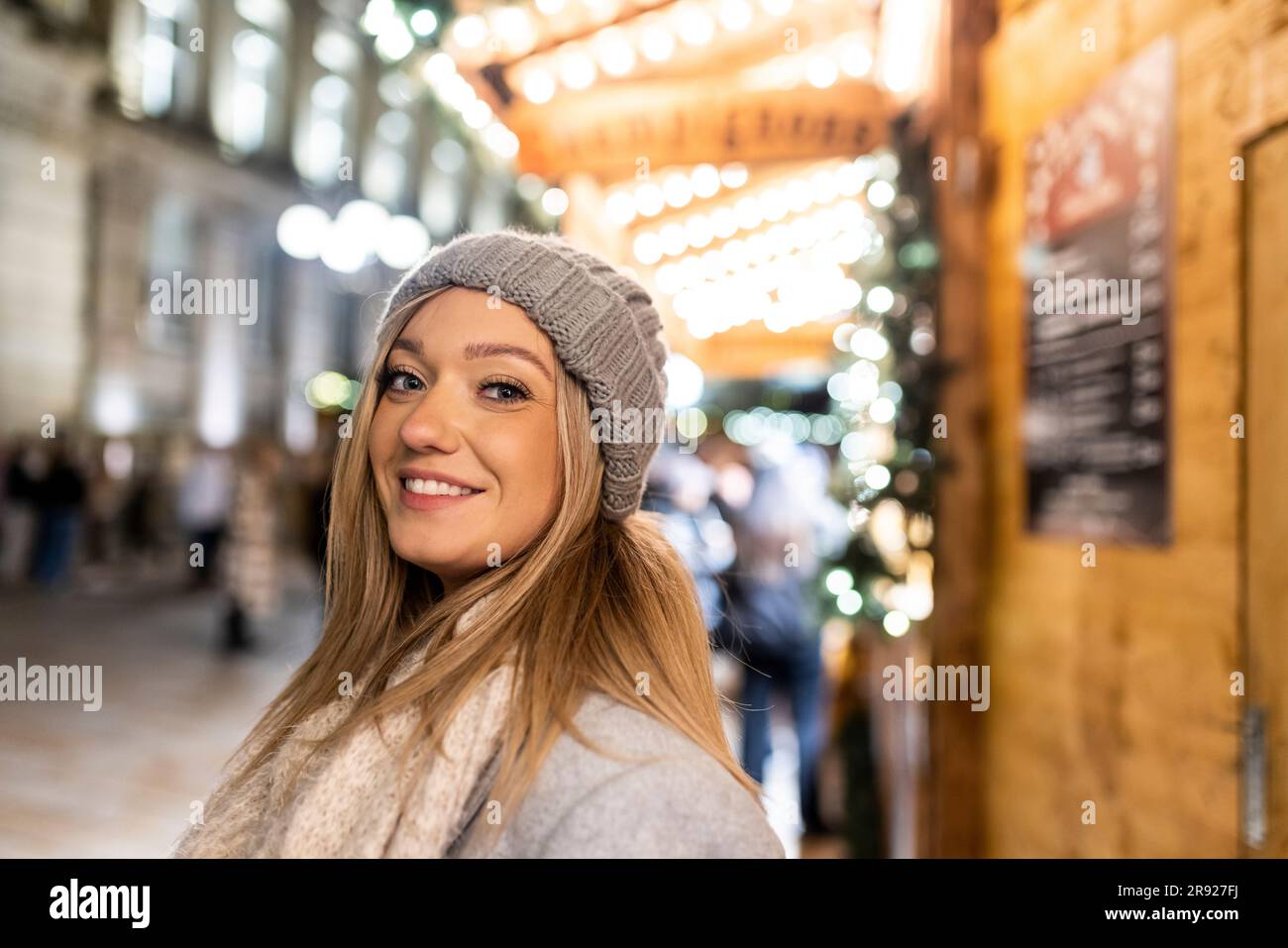 Giovane donna felice che indossa un cappello in maglia al mercatino di Natale Foto Stock