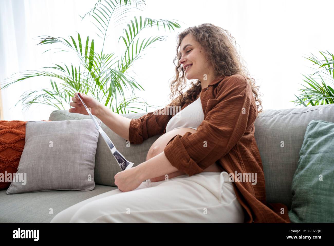 Donna incinta sorridente che guarda le foto ecografiche seduto sul divano Foto Stock