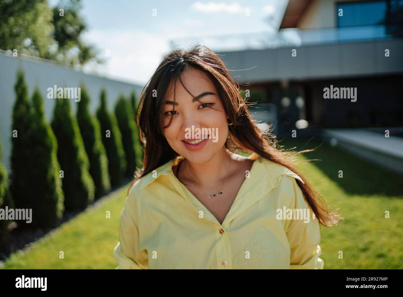 Donna sorridente nel cortile di casa in una giornata di sole Foto Stock