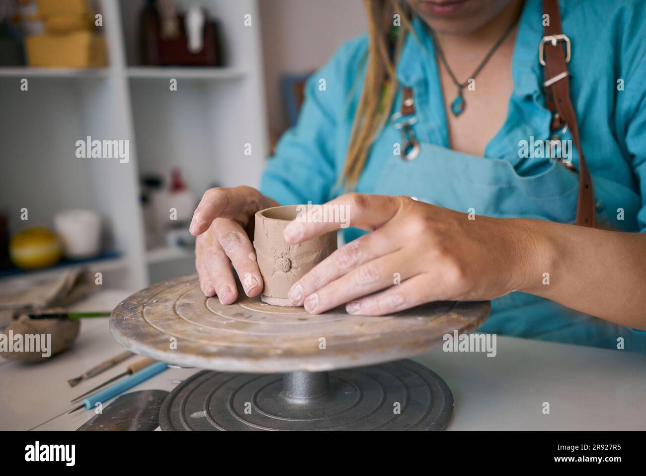 Artigiana che scolpisce una tazza di argilla su una ruota in ceramica presso l'officina Foto Stock