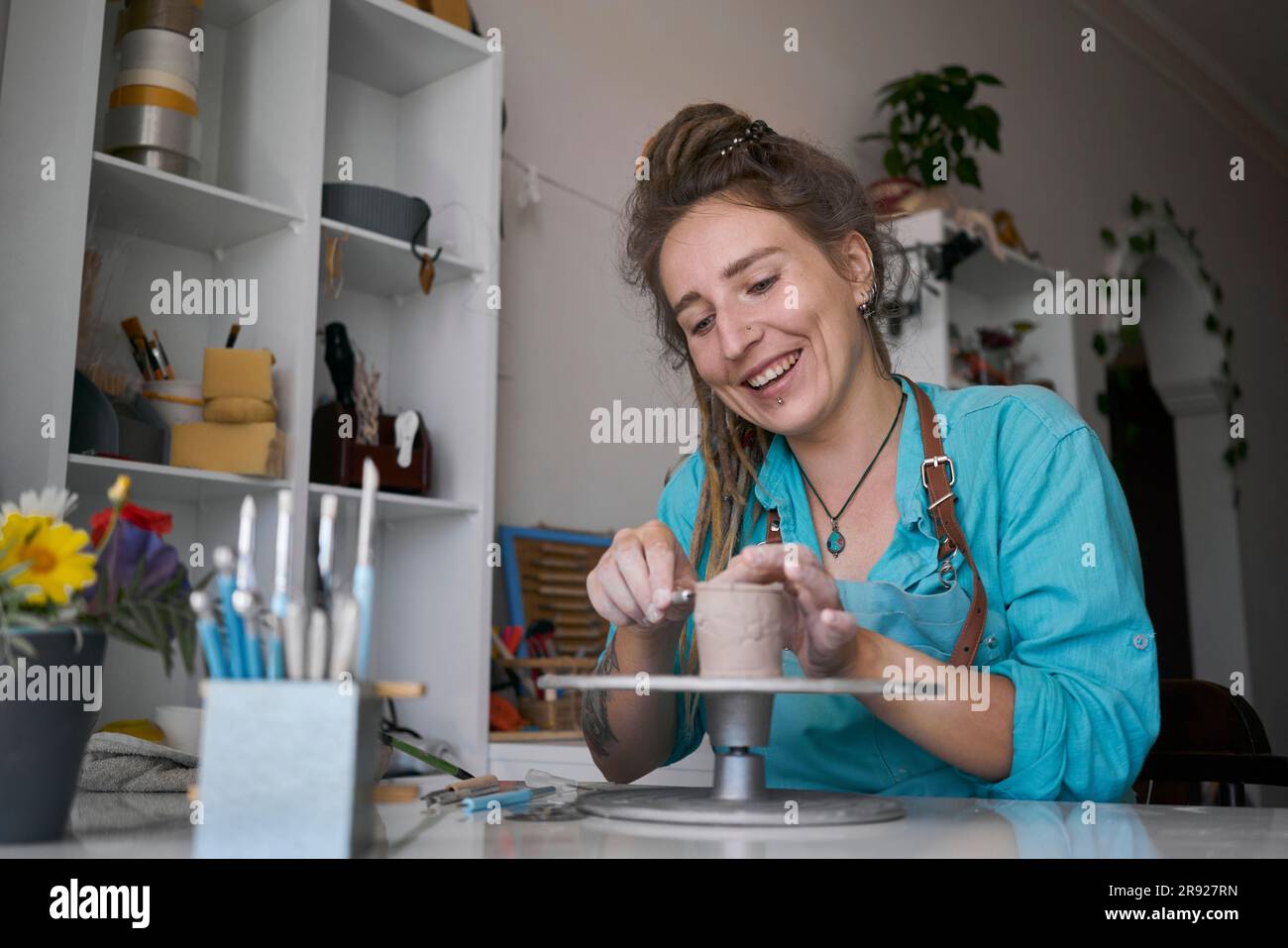 Donna felice che scolpisce una tazza di argilla in officina Foto Stock