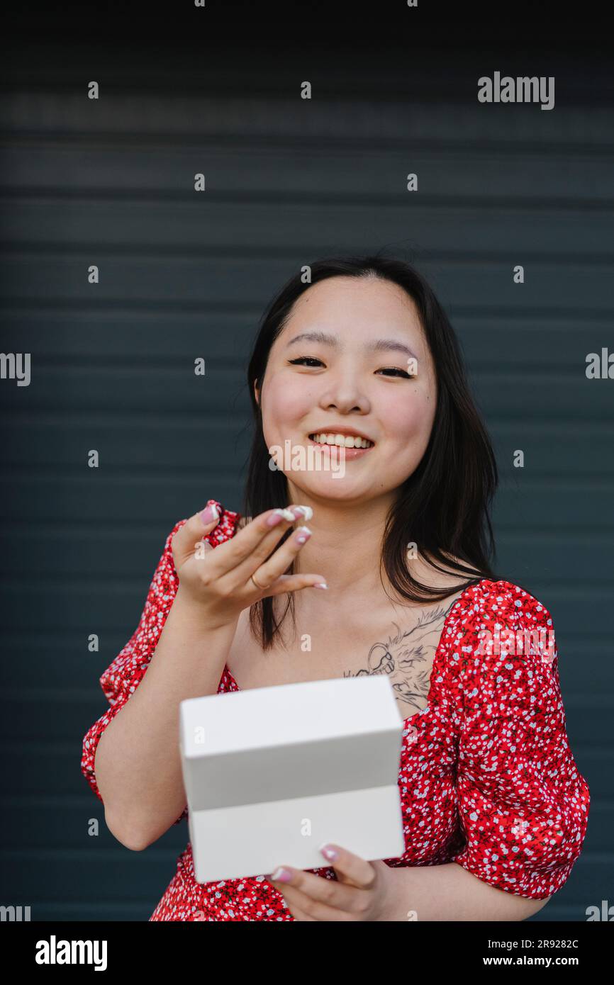 Giovane donna che tiene una scatola davanti all'otturatore chiuso Foto Stock