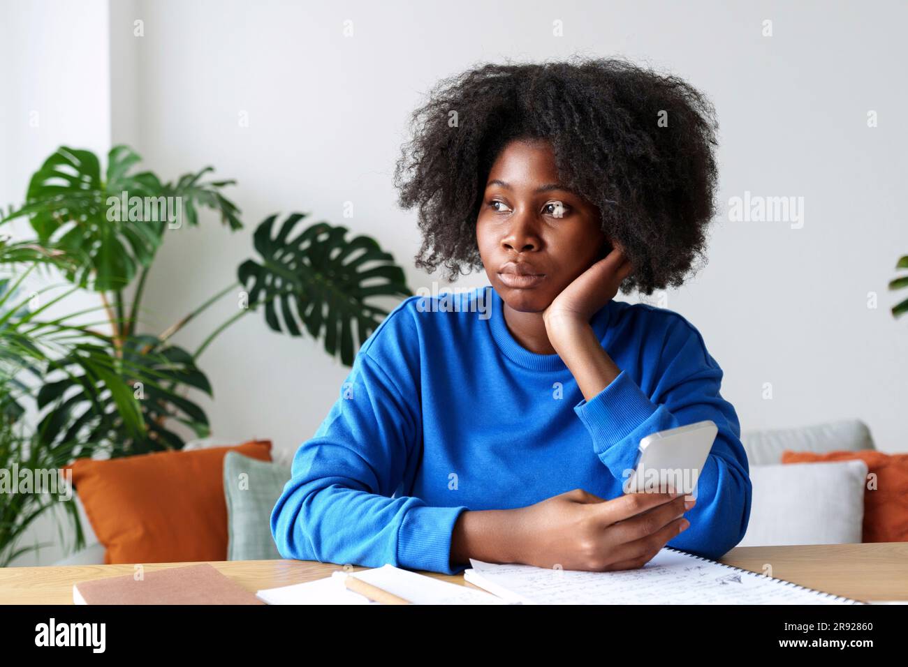 Donna afro premurosa che ha in mano le finanze domestiche di pianificazione di smartphone Foto Stock