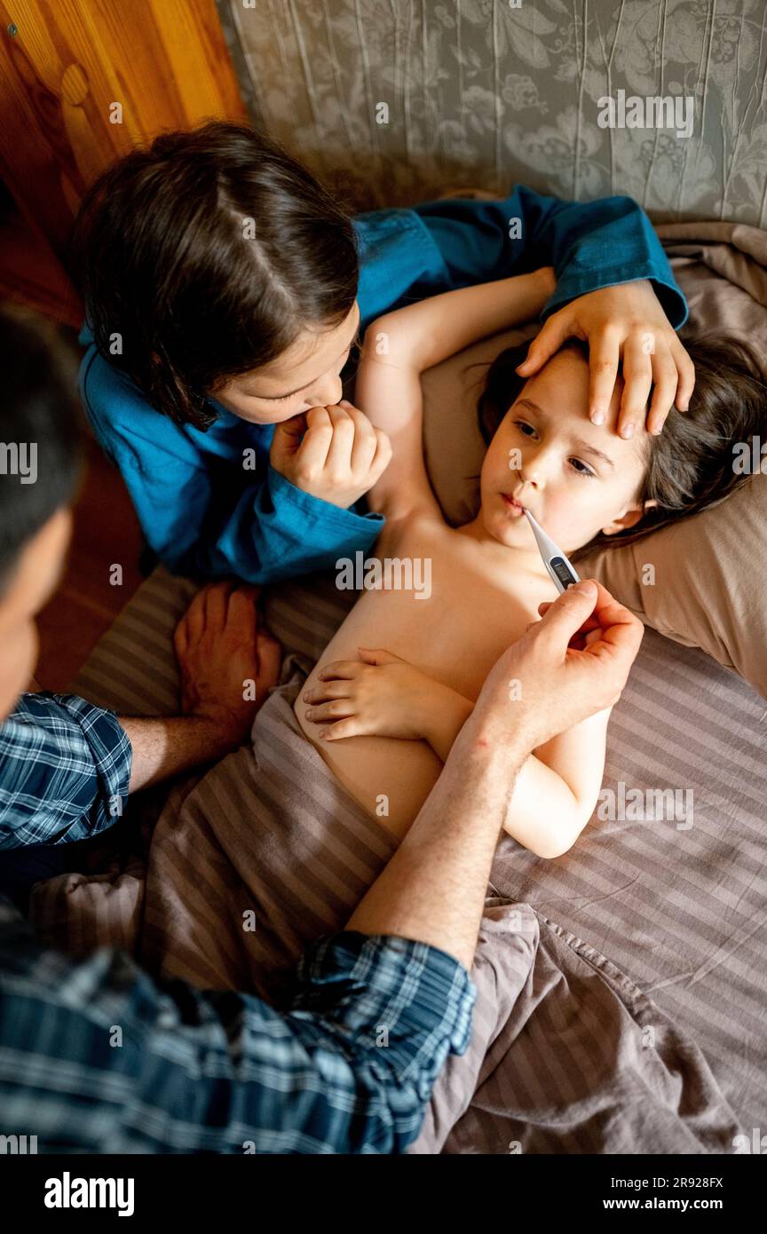 Padre che controlla la temperatura del bambino malato con il termometro a casa Foto Stock