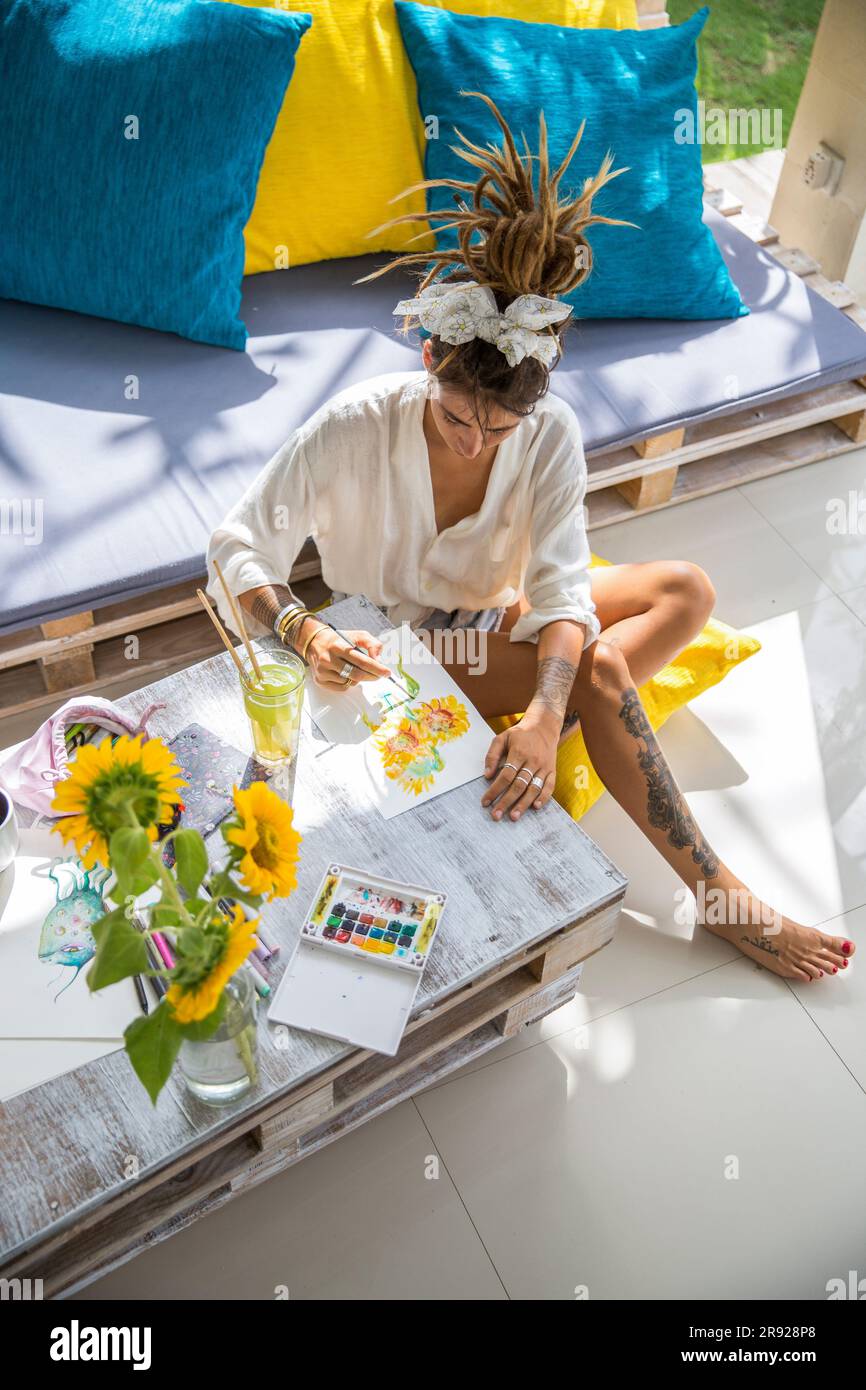 Artista che dipinge fiori su carta seduto a casa Foto Stock