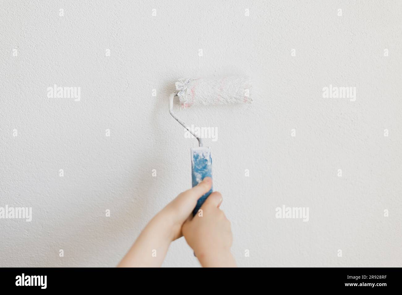 Mano di ragazzo dipinge parete bianca usando il rullo a casa Foto Stock