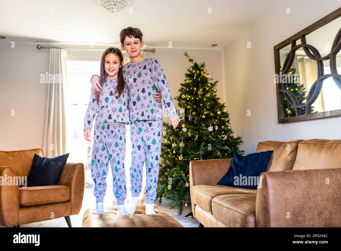 Buon fratello e sorella in piedi sul tavolo in salotto a casa nel periodo natalizio Foto Stock