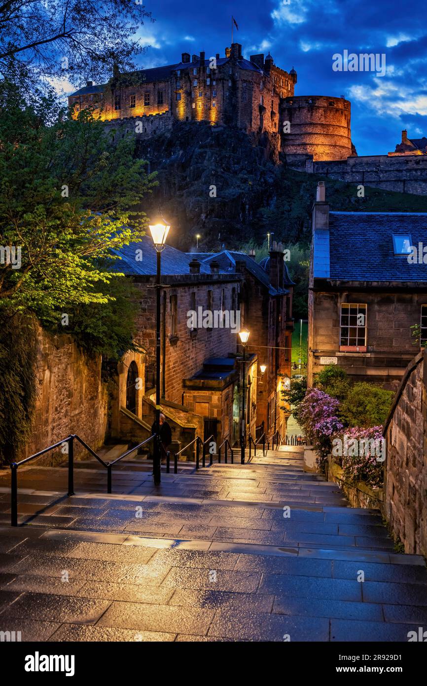 Regno Unito, Scozia, Edimburgo, luci di strada illuminano i vicoli vuoti al crepuscolo con il Castello di Edimburgo sullo sfondo Foto Stock
