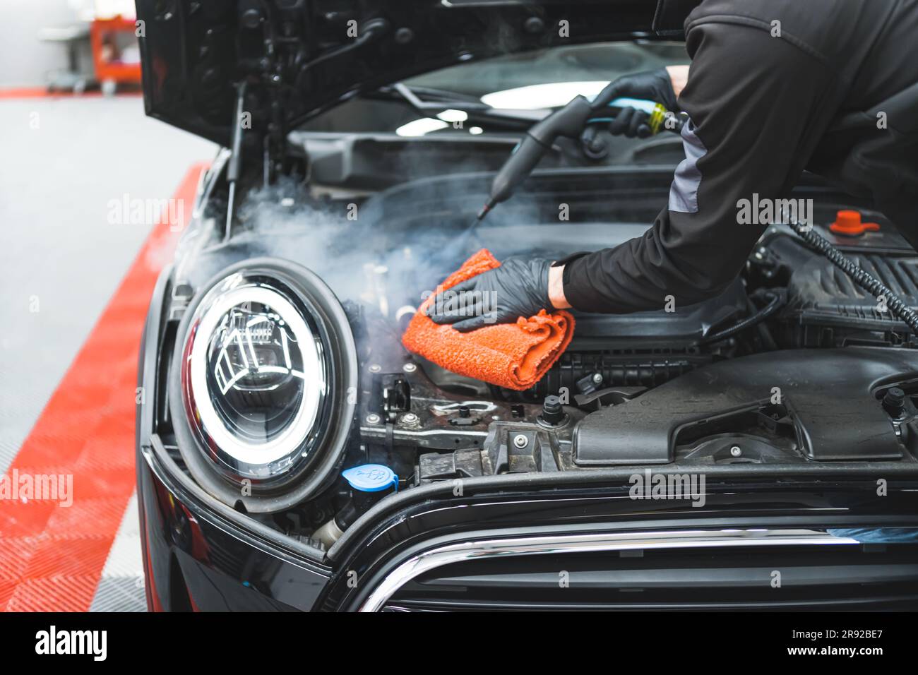 Concetto di dettaglio dell'auto. Pulizia manuale del motore con vapore. Esperto di dettagli per auto, pulizia profonda del veicolo nero e pulizia della superficie dell'auto con un panno in microfibra arancione. Foto di alta qualità Foto Stock