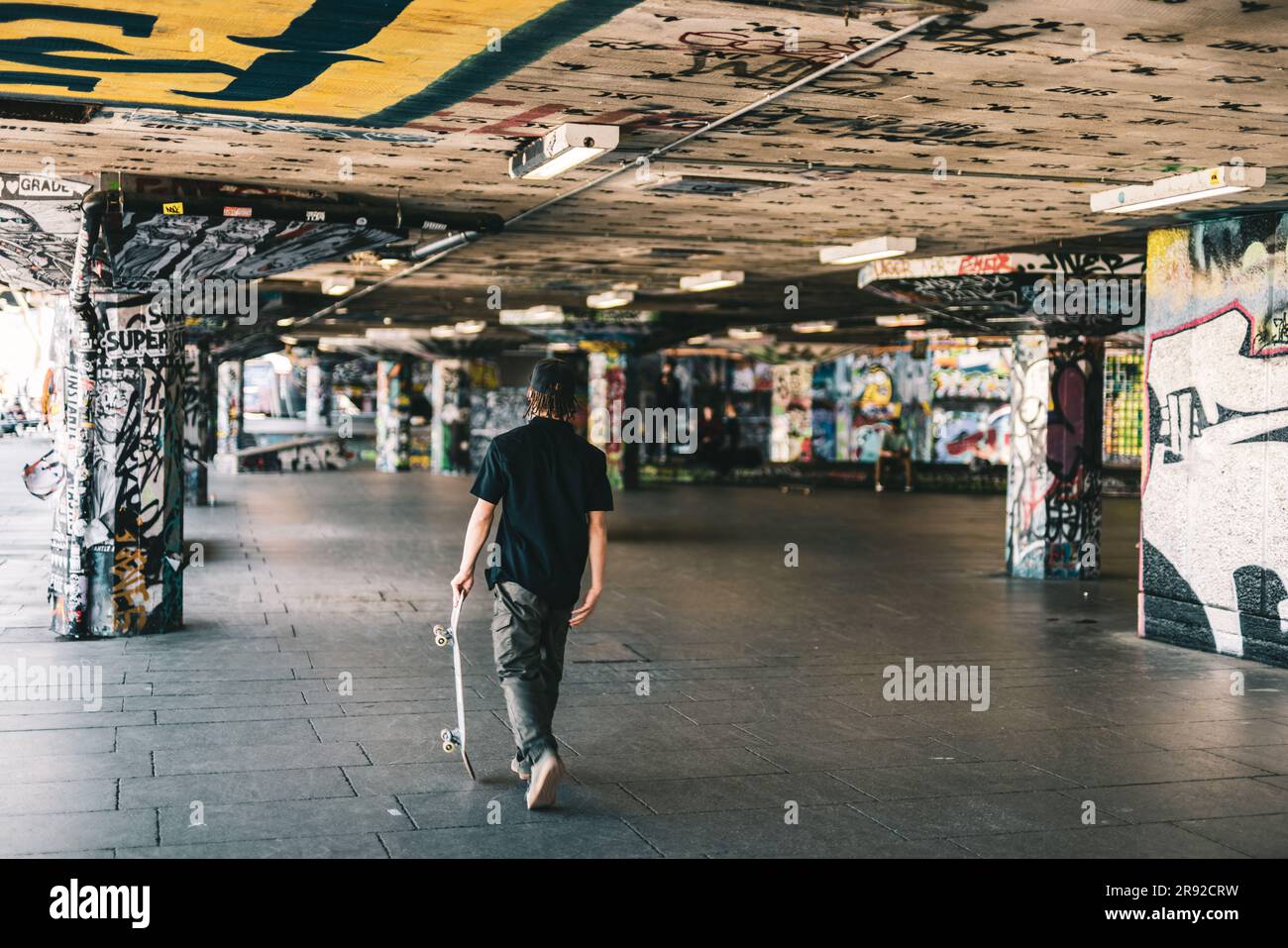 Un uomo sta passeggiando in una camera sotterranea buia e abbandonata con uno skateboard Foto Stock