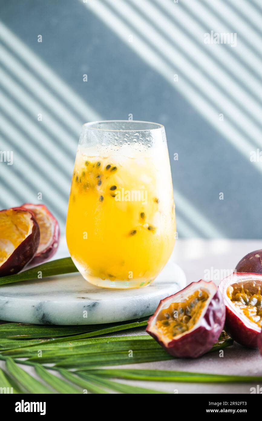 Bicchiere di bibita alla frutta della passione Iced con limone e mezza fetta di frutto della passione su sfondo leggero, bevanda rinfrescante o bevanda con ghiaccio Foto Stock