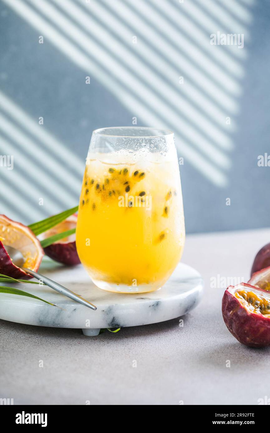 Bicchiere di bibita alla frutta della passione Iced con limone e mezza fetta di frutto della passione su sfondo leggero, bevanda rinfrescante o bevanda con ghiaccio Foto Stock