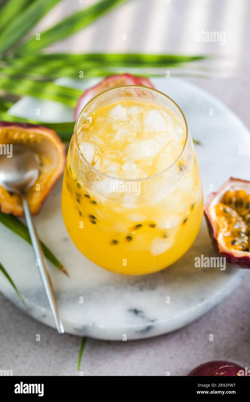 Bicchiere di bibita alla frutta della passione Iced con limone e mezza fetta di frutto della passione su sfondo leggero, bevanda rinfrescante o bevanda con ghiaccio Foto Stock
