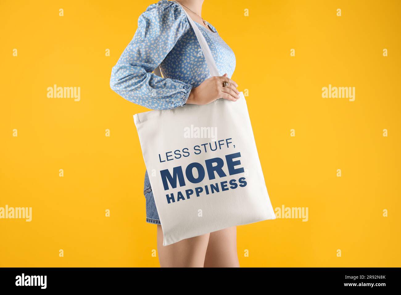 Vibrazioni motivazionali. Donna che tiene una borsa in tessuto con frasi meno roba più felicità su sfondo giallo, primo piano Foto Stock