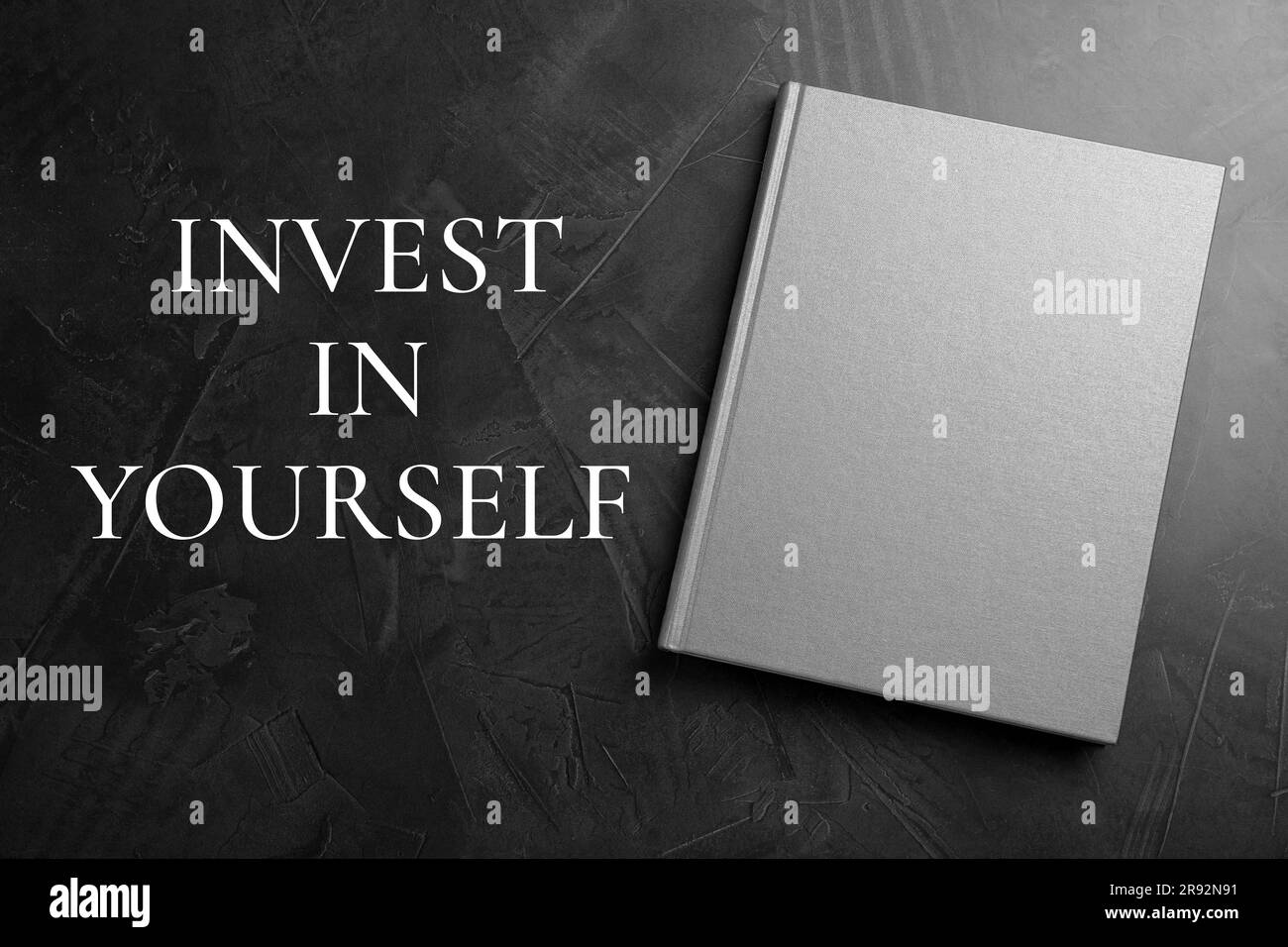Investite in voi stessi, affermazione. Libro e parole sul tavolo nero, vista dall'alto Foto Stock