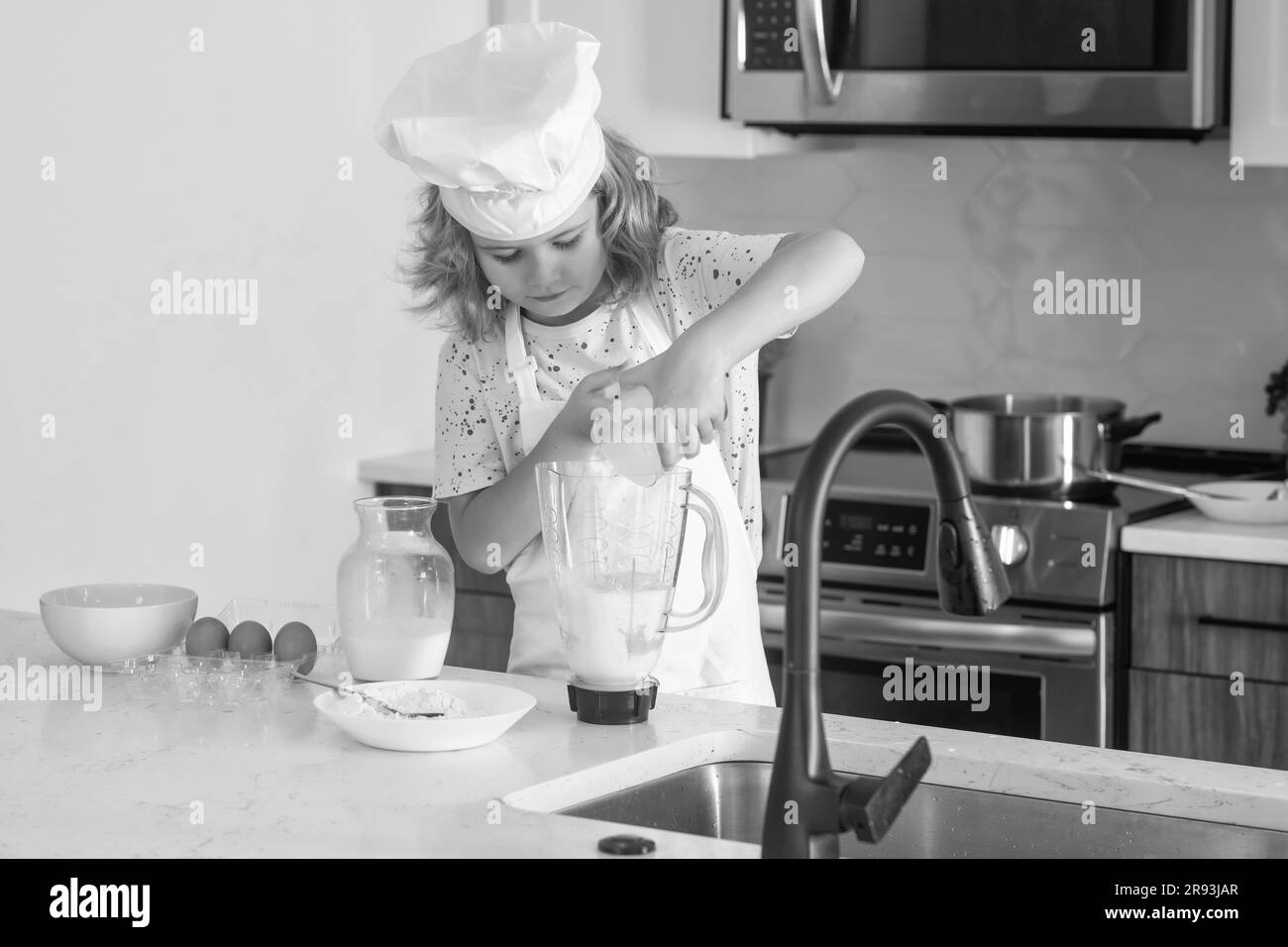 Cuoco del cuoco del capretto sta imparando come fare una torta nella cucina domestica. Bambino che rende gustoso delizioso. Uova, latte e farina ingredienti per la cottura dei biscotti o. Foto Stock