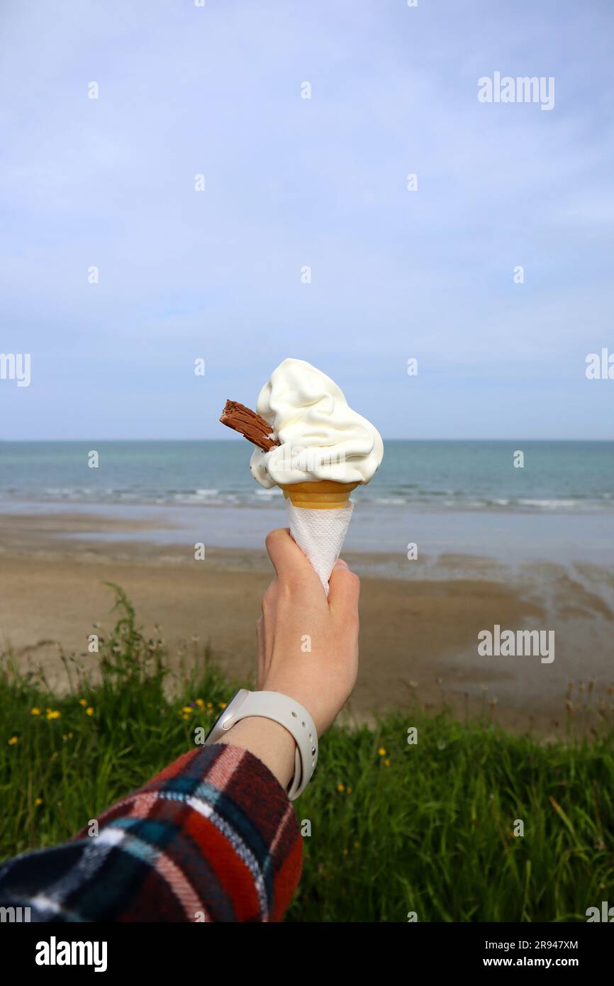 Mano allungata con gelato bianco con bastoncino di cioccolato sullo sfondo del mare blu in una giornata di sole estivo Foto Stock