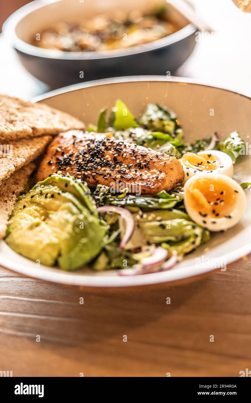 Insalata di foglie fresche servita con avocado, uova e salmone alla griglia in cima costellato di sesamo. Foto Stock