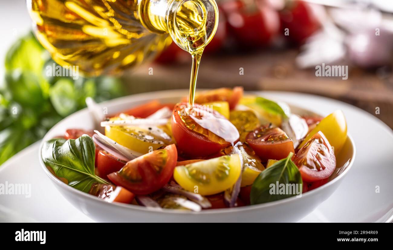 L'olio d'oliva viene versato sull'insalata di pomodoro fresco mescolata con cipolla rossa. Foto Stock