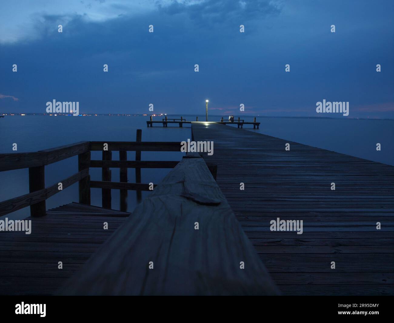 Cieli scuri al crepuscolo lungo un molo di Barnegat Bay, New Jersey. Le luci distanti allineano l'area costiera. Foto Stock
