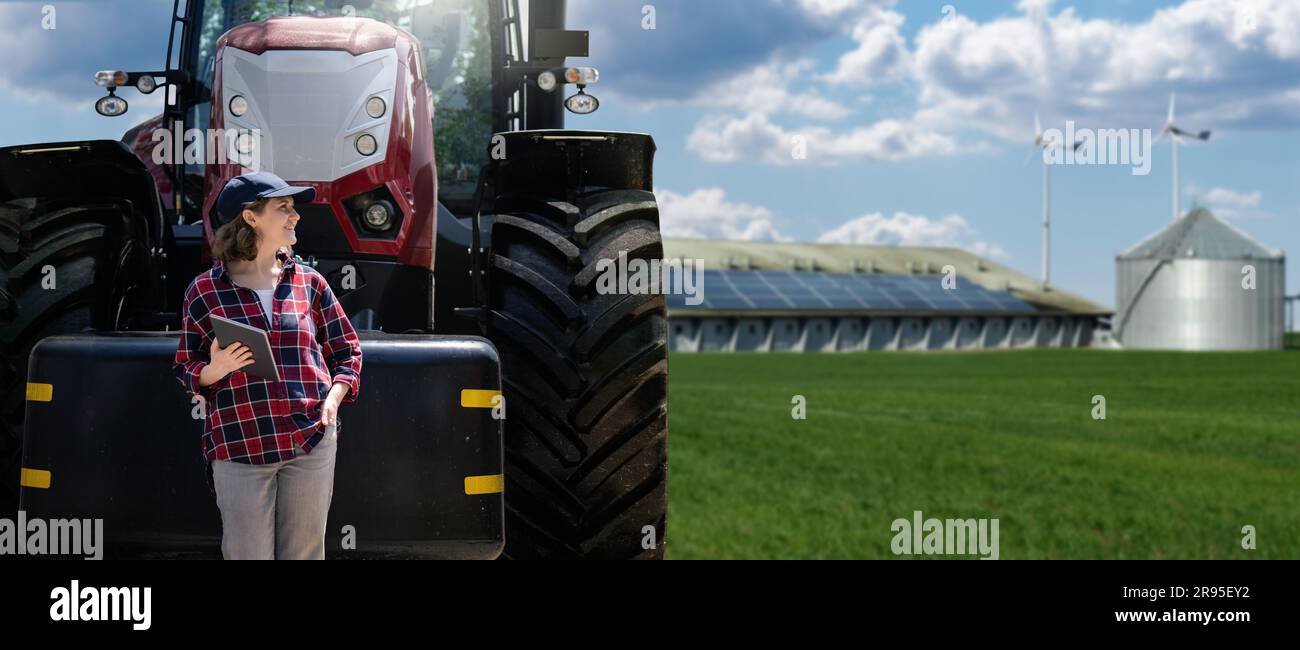 Donna contadina con un tablet digitale e un trattore agricolo sullo sfondo di un'azienda agricola moderna. Foto Stock