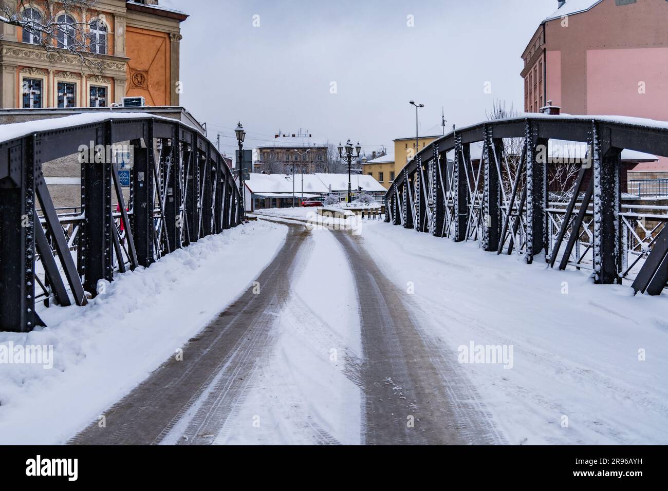 Klodzko, Polonia - gennaio 2023: Piccolo ponte con parti di costruzione in metallo nero sopra un piccolo fiume pieno di neve in inverno Foto Stock