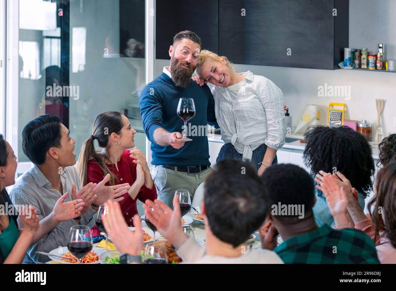Felice coppia giovane che si diverte comunicando e brindando con gli amici nella sala da pranzo. amici applaudono. Foto Stock