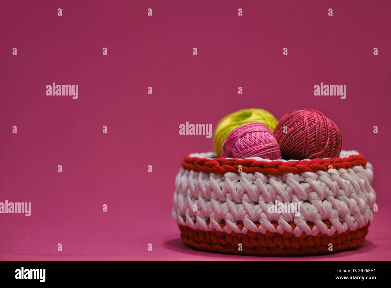 Concept hobby artigianale per ricci da casa. Filati per uncinetto. Diverse palline di lana multicolore di filo in un cestino di vimini su un dorso rosa Foto Stock