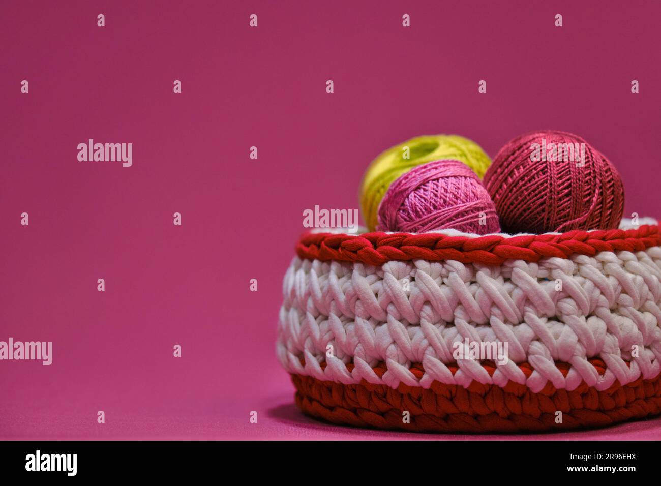 Concept hobby artigianale per ricci da casa. Filati per uncinetto. Diverse palline di lana multicolore di filo in un cestino di vimini su un dorso rosa Foto Stock