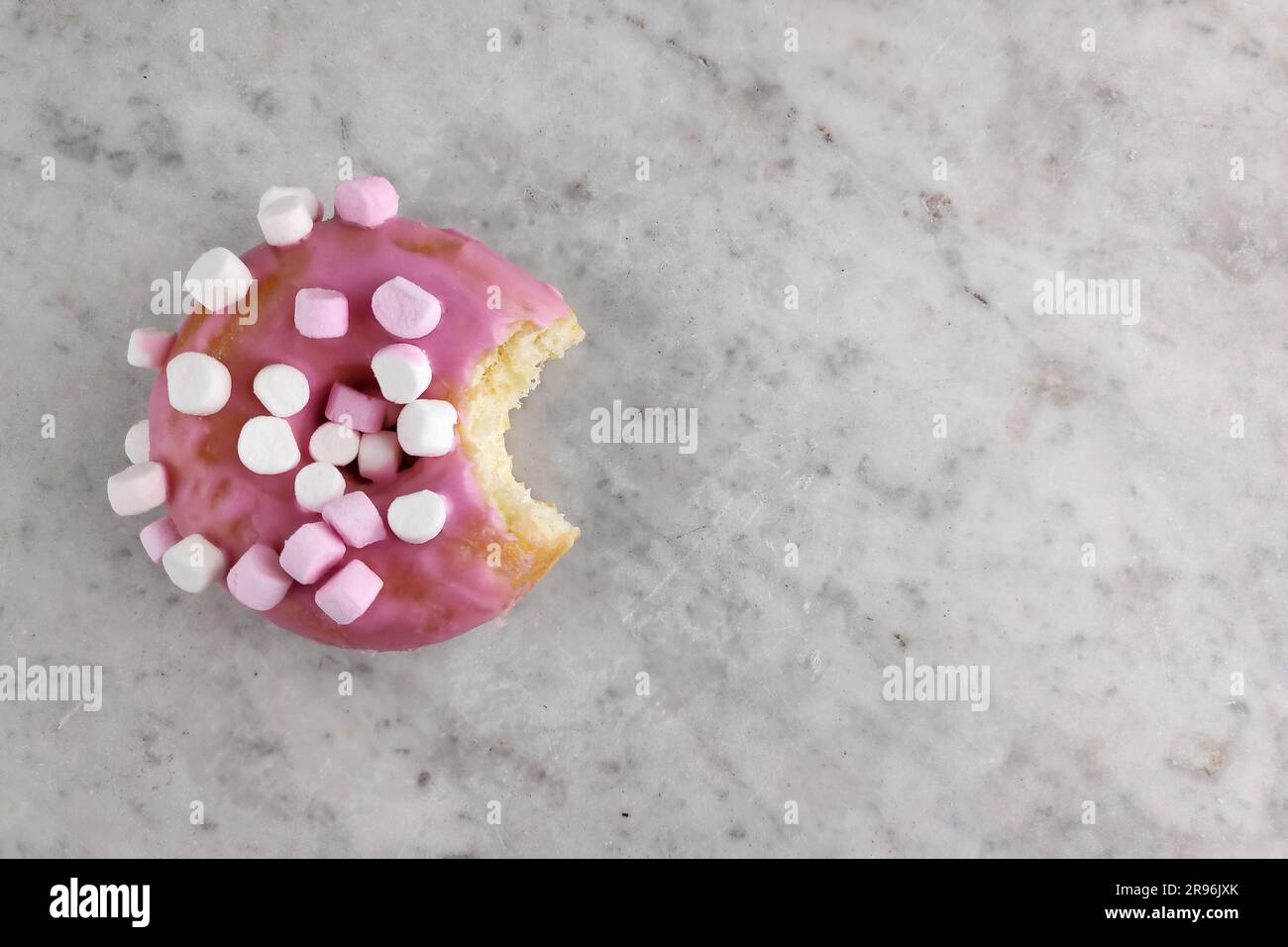 Ciambella con glassa rosa e marshmallow piccoli con un boccone mancante. Foto Stock