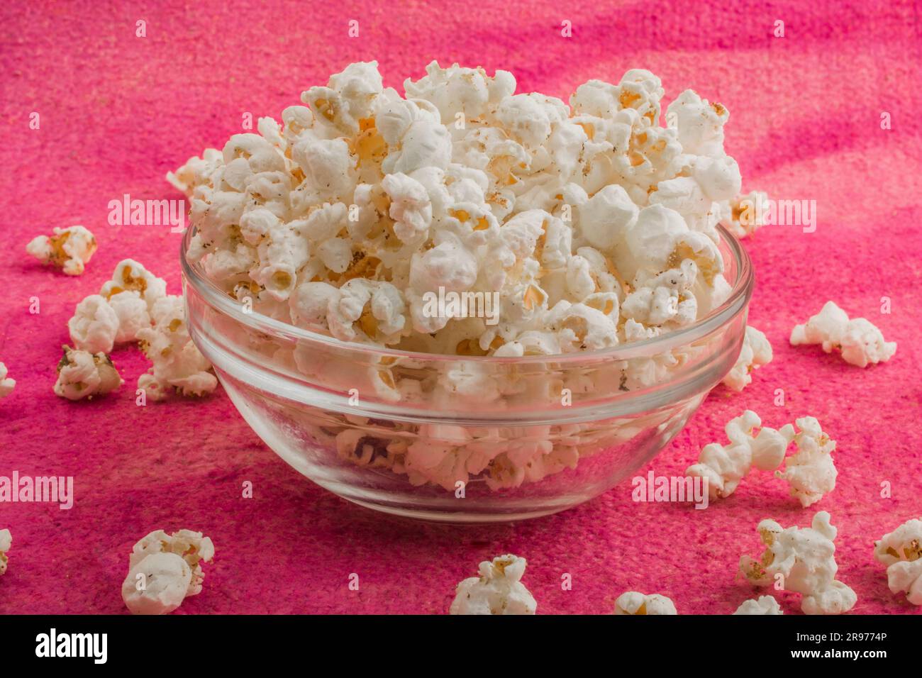 popcorn in un piatto di vetro, su uno sfondo rosa irregolare Foto Stock