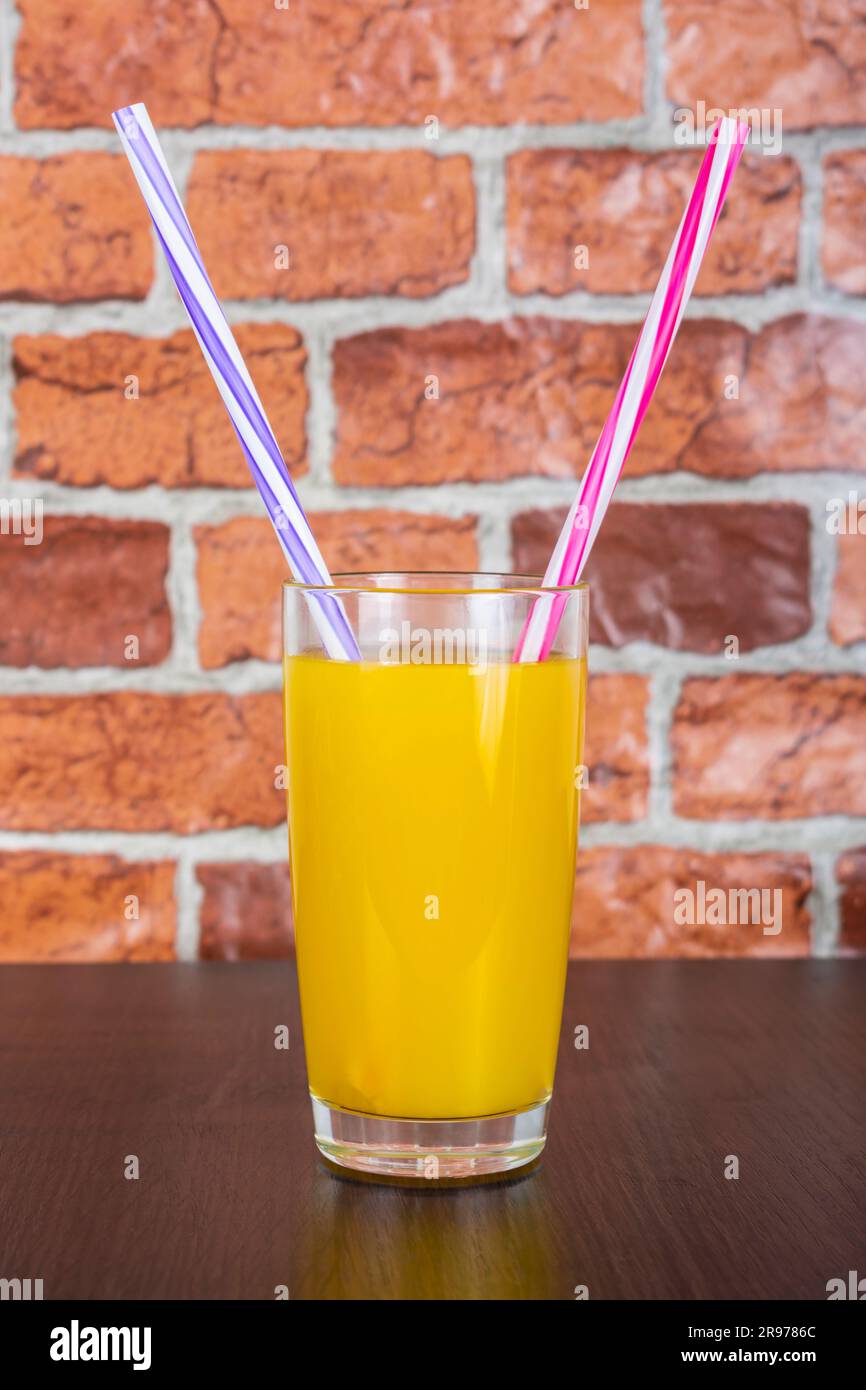 Succo d'arancia in un bicchiere con due tubi vitamine concetto di salute sfondo di legno e una parete di mattoni sullo sfondo Foto Stock